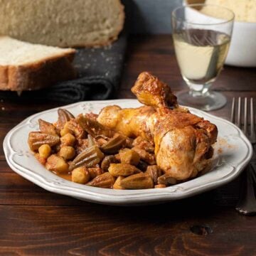 Okra stew with chicken on a plate with bread and a glass of wine on the side.