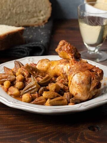 Okra stew with chicken on a plate with bread and a glass of wine on the side.