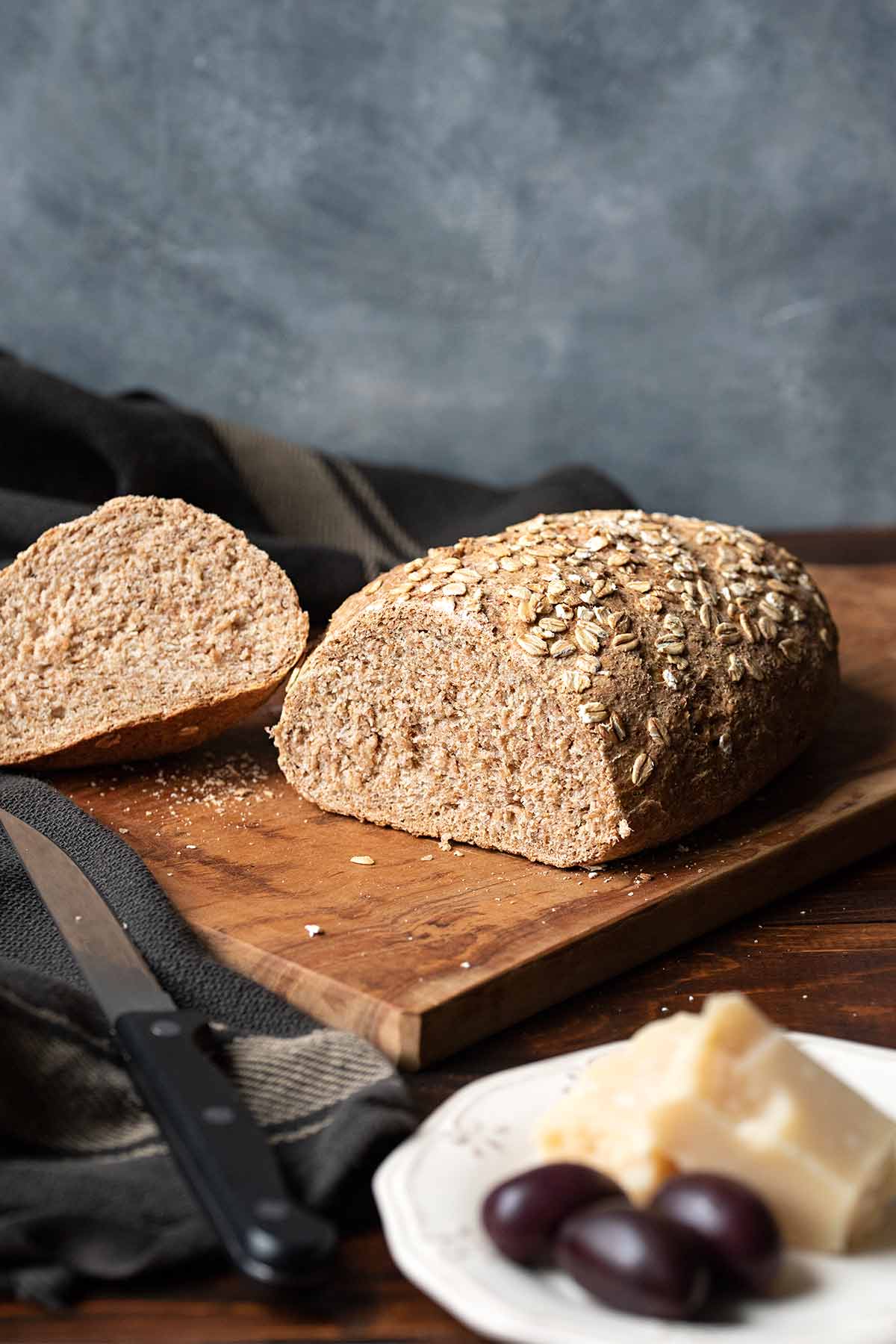 Whole wheat bread on a cutting board, a towel and a knife.
