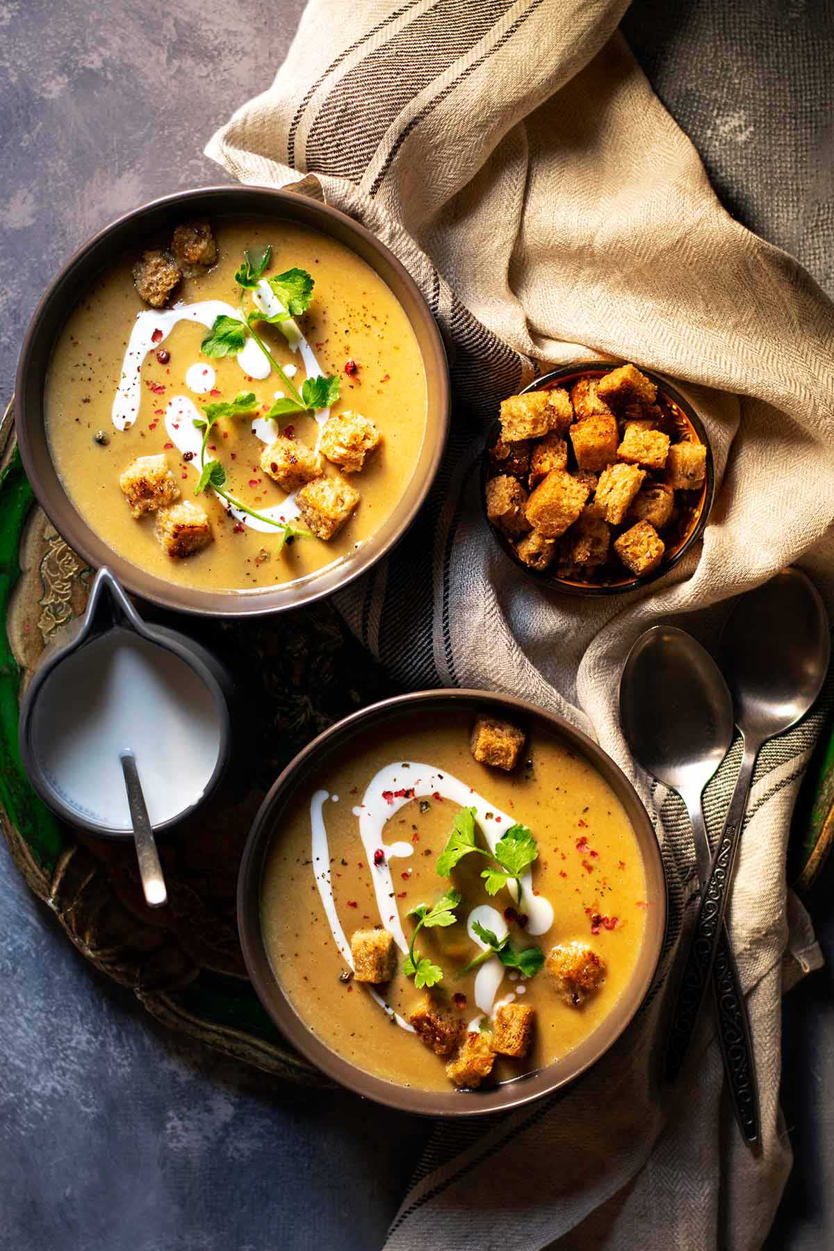 Two bowls of vegan pumpkin soup with coconut cream and red lentils.