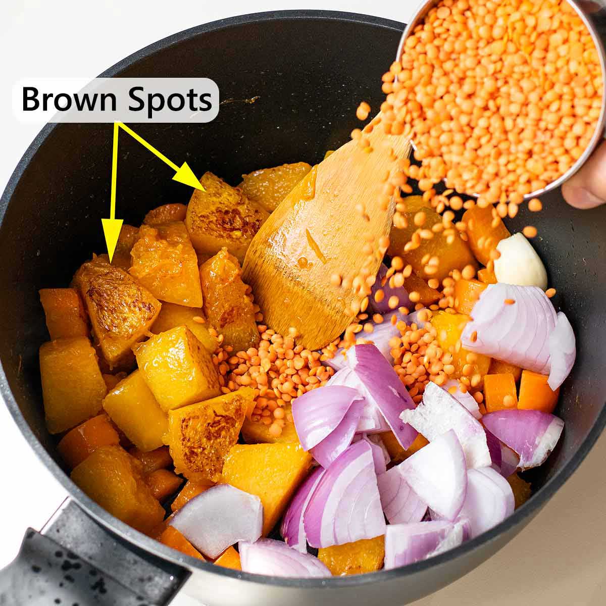 Adding the red lentils into the pot with the sauteed pumpkin.