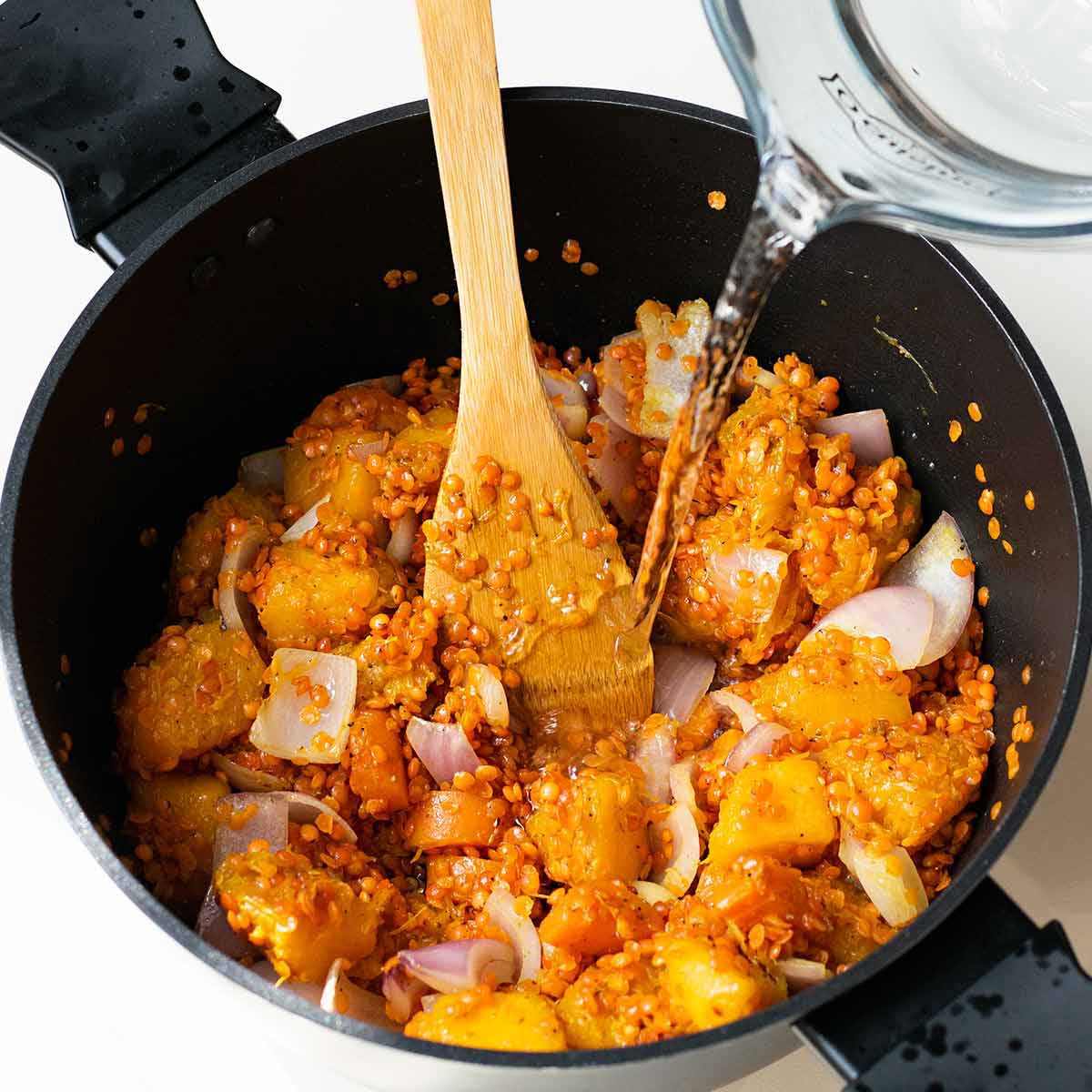 Adding water into the pot with the pumpkin and red lentils.