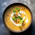 A bowl of pumpkin soup with red lentils and coconut milk garnished with pink peppercorns and Mediterranean hartwort.