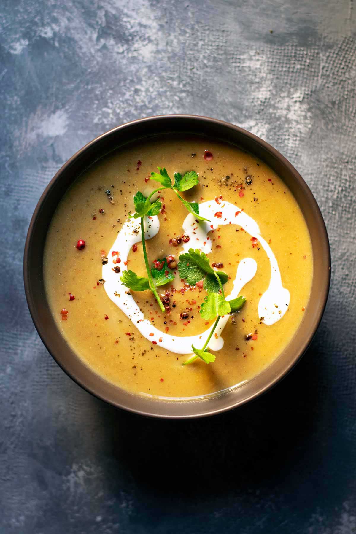 A bowl of pumpkin soup with red lentils and coconut milk garnished with pink peppercorns and Mediterranean hartwort.
