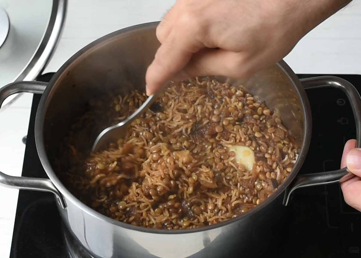 A metal fork fluffing up the Mujadara in the pot.