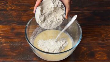 A hand adding flour to a bowl with milk.