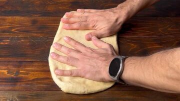 Two hands spreading cinnamon roll dough on a wooden surface.