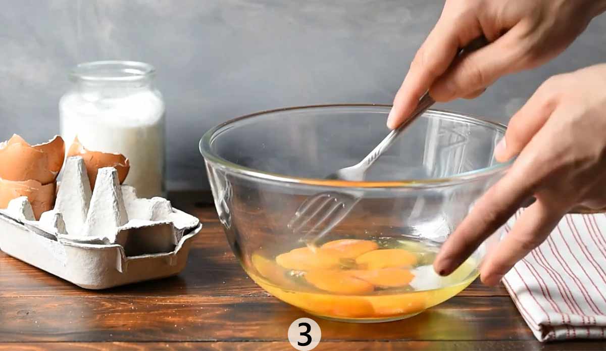 Two hands beating egg in a bowl with a fork.
