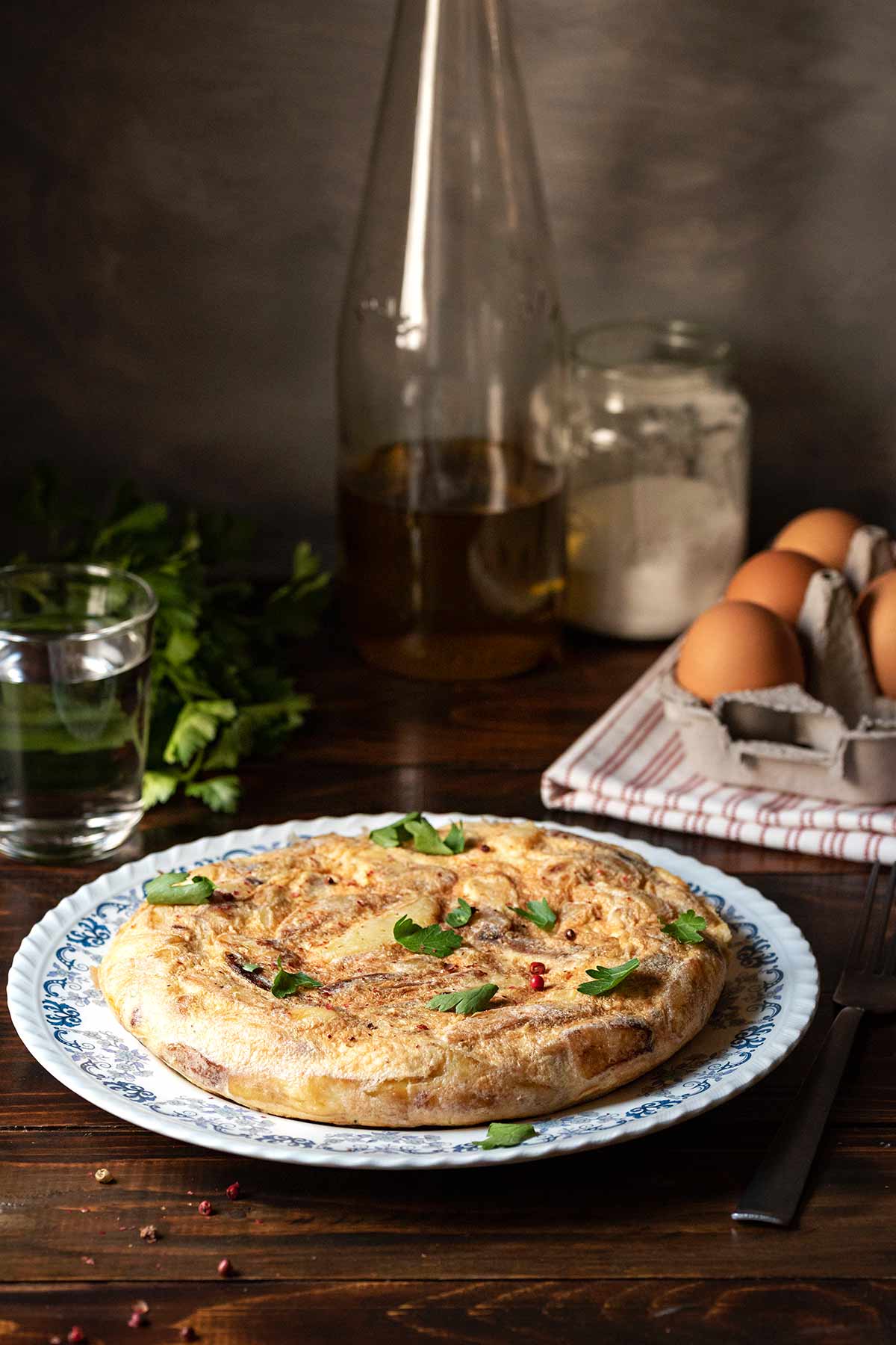 Spanish potato omelette served on a plate, next to fresh eggs and a bottle of olive oil.
