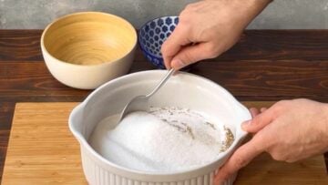 A hand mixing salt and sugar in a container.