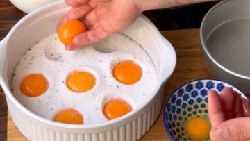 A hand placing the yolks in the curing mixture.