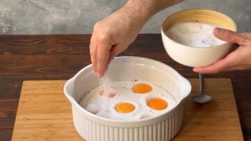 A hand sprinkling salt over the yolks.