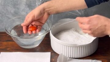 A hand dipping the cured yolks in a bowl with water.