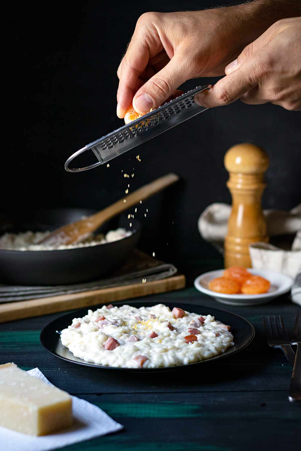 Two hands grating an firm yolk over a plate with risotto.