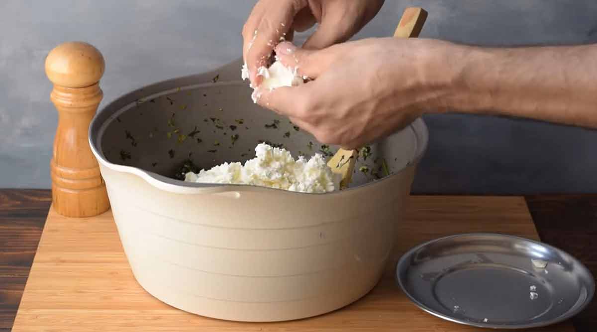Two hands adding feta cheese to the spinach mixture.