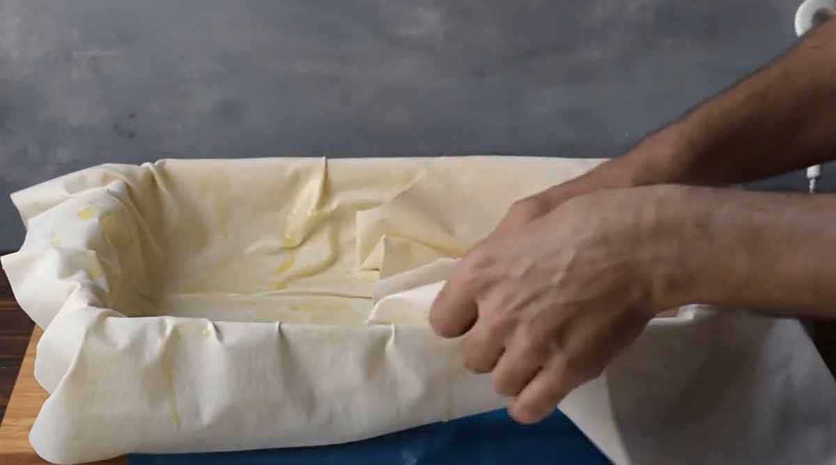 Two hands layering phyllo dough sheets to the baking dish.