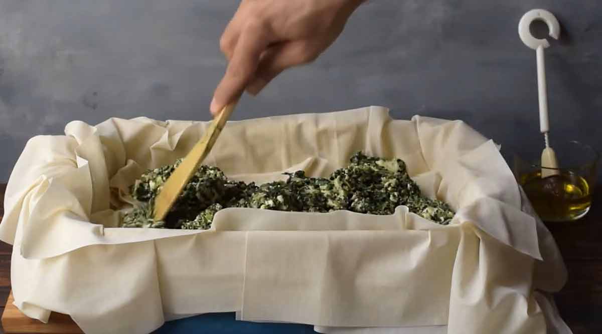A hand adding the spinach filling over the phyllo.