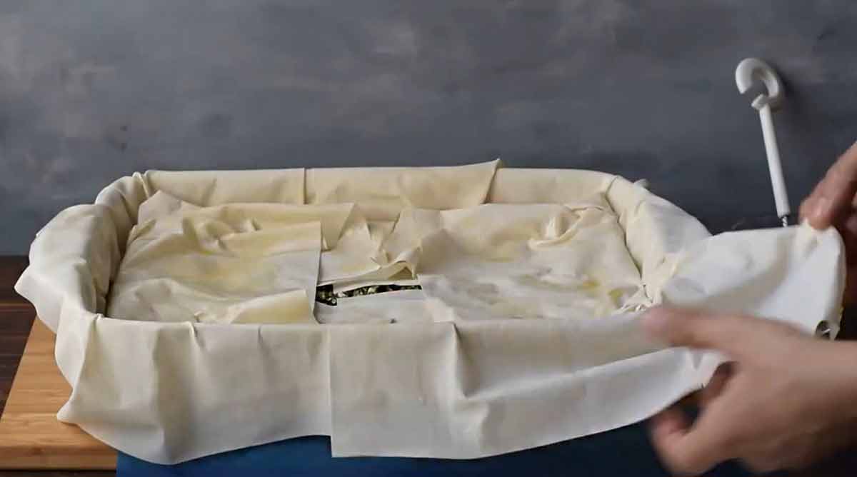 A hand folding the phyllo sheets over the filling.
