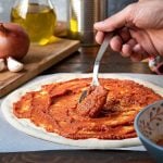 spooning pizza sauce on dough.