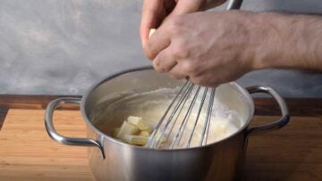 Two hands adding white chocolate to hot custard in a pot.