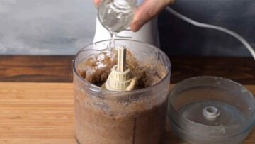 A hand adding water to chestnut purée in a food chopper.
