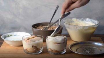 A hand adding custard cream to glasses with savoiardi biscuits and chestnut purée.