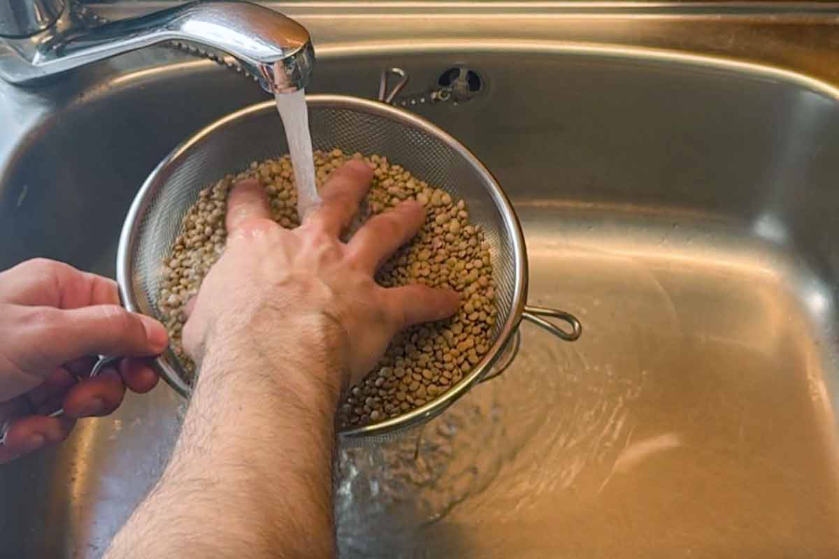 A hand rinsing lentils inside a sieve.