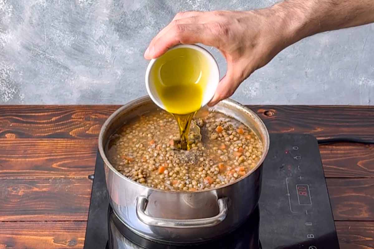 A hand adding olive oil to the pot.