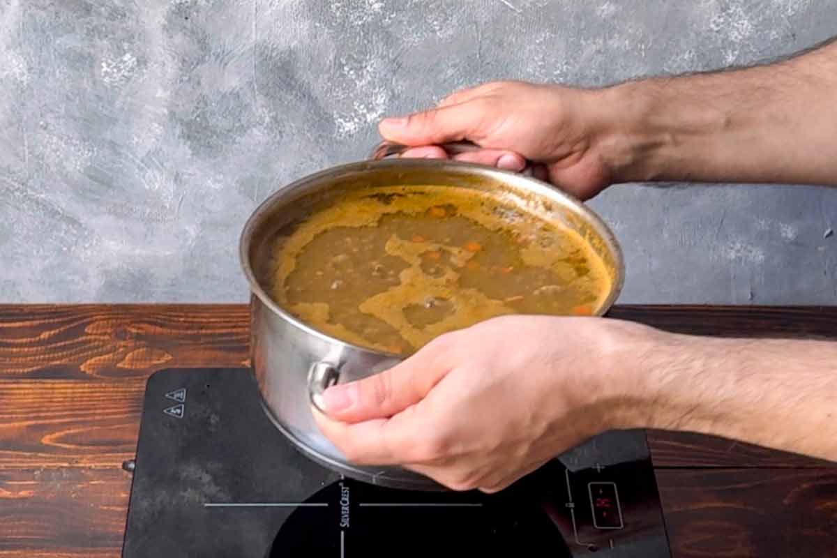 Two hands taking the pot off the stove.