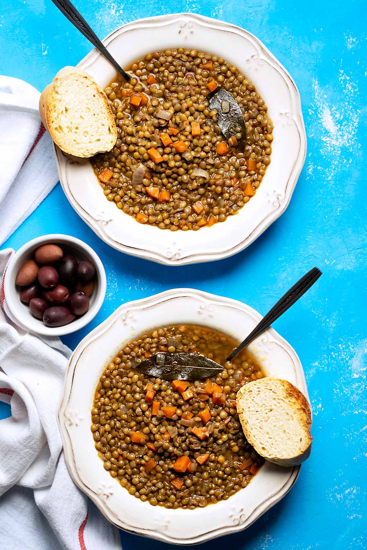 Two plates with Greek lentil soup, a bowl with olives and two slices of bread.
