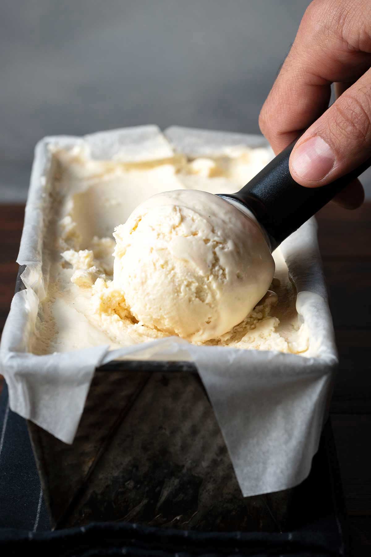 Scooping homemade vanilla ice cream recipe from a loaf pan.