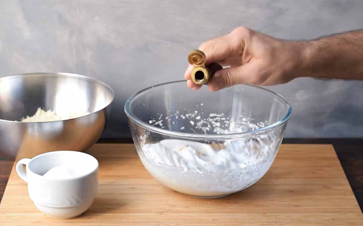 A hand adding almond extract to the egg whites.