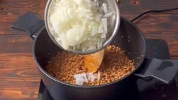 A hand adding chopped onion to the pot.
