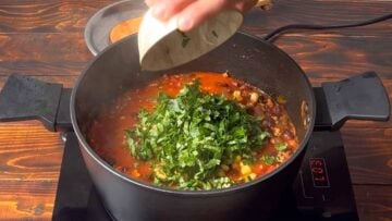 A hand adding chopped parsley to the pot.