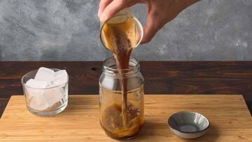 A hand pouring espresso coffee in a glass.
