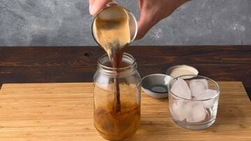 A hand pouring espresso coffee in a jar.