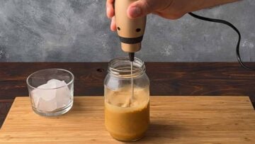A hand mixing the coffee with a frother.