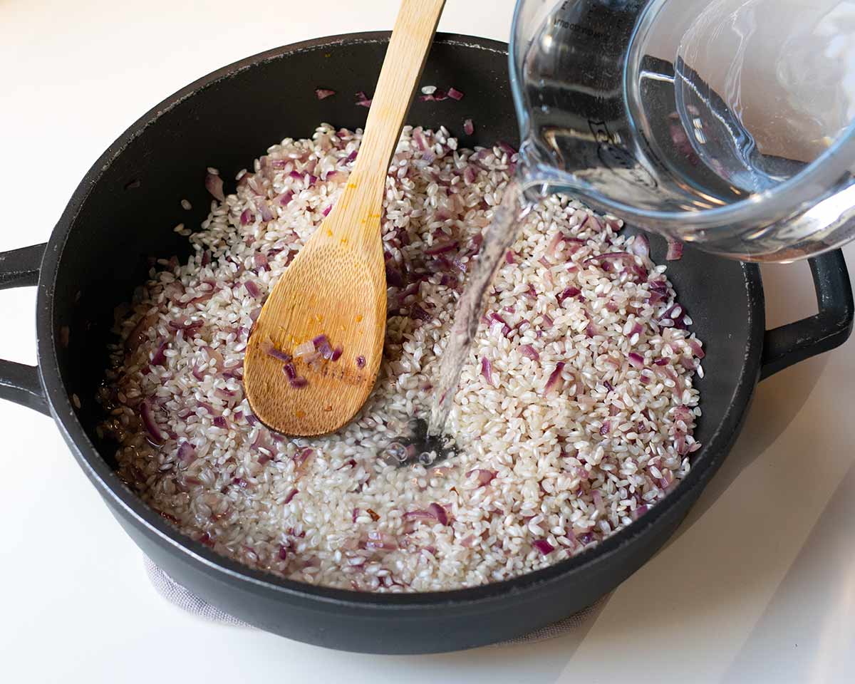 A hand pouring water in the skillet with the rice.