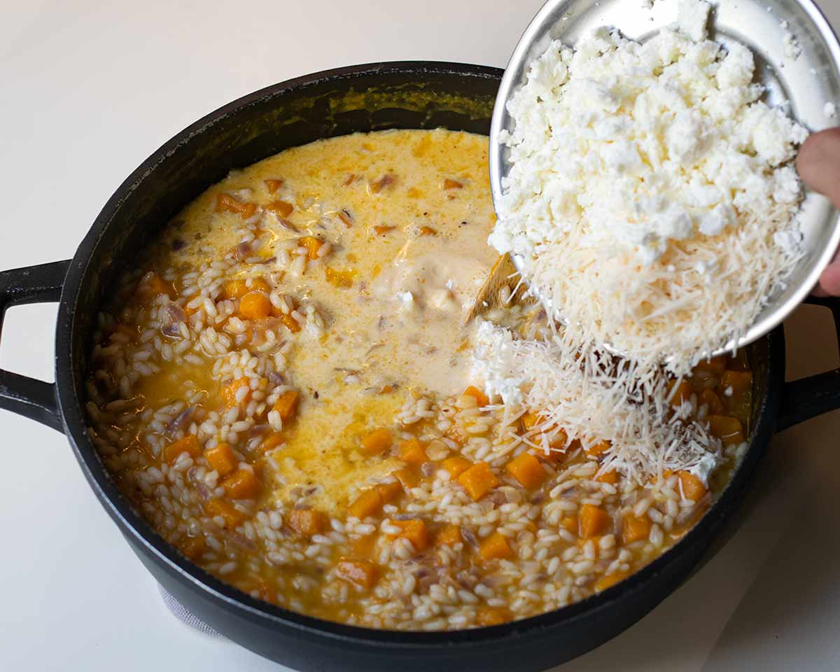 A hand transferring the feta and Parmesan into the skillet.