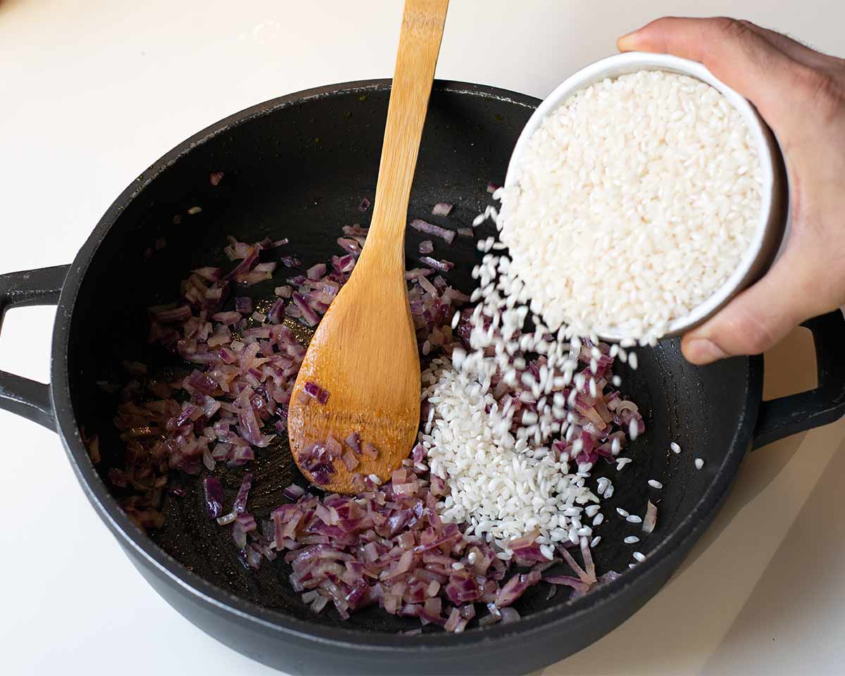 A hand transferring the rice into the skillet.