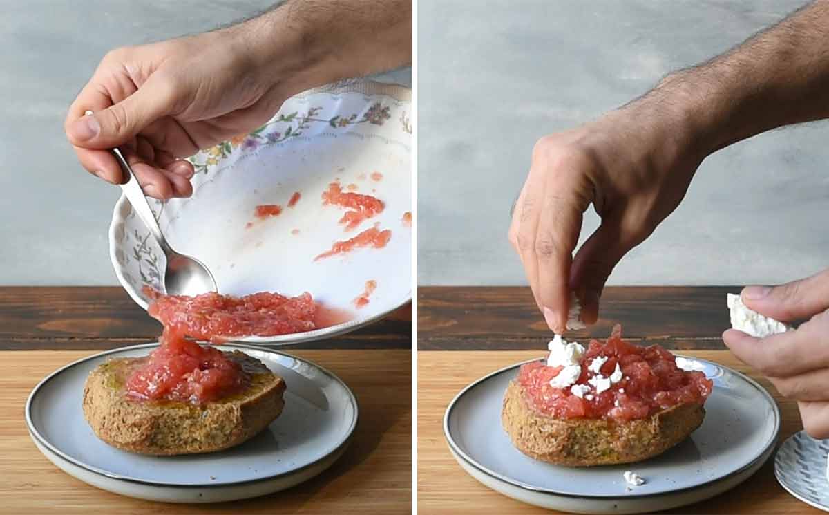 A hand adding grated tomato and feta cheese to a barley rusk.