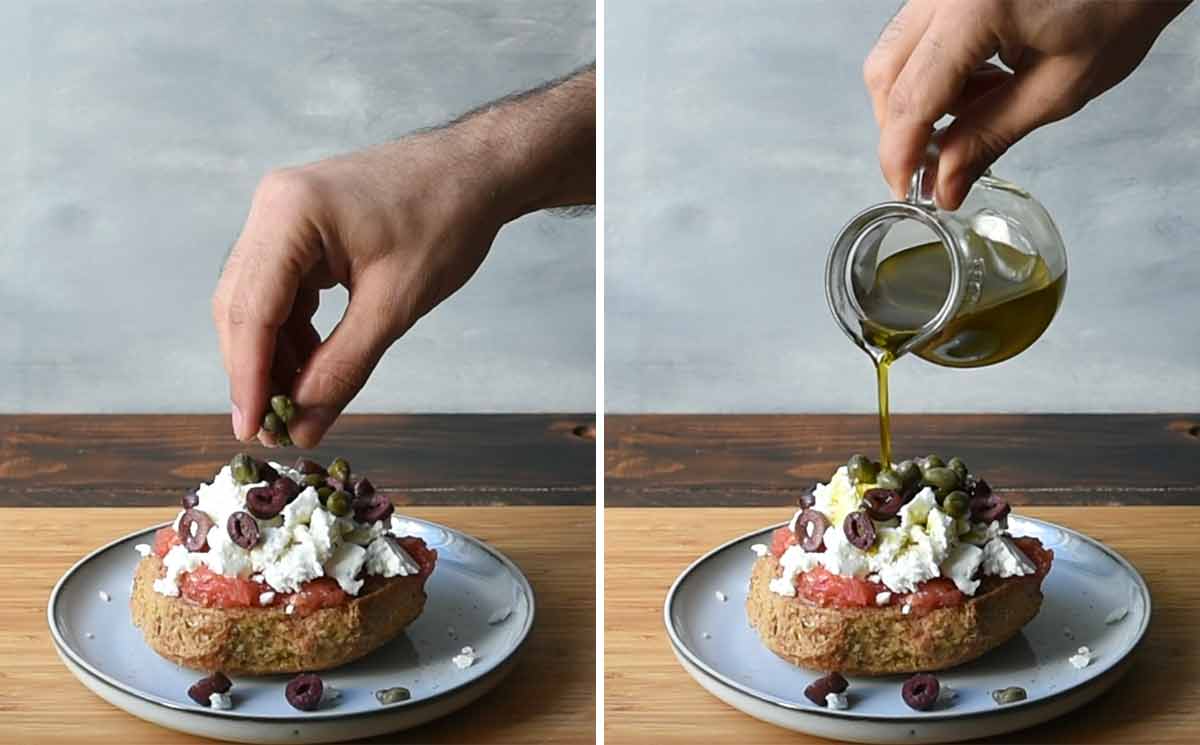A hand adding olives and olive oil on top of a barley rusk.