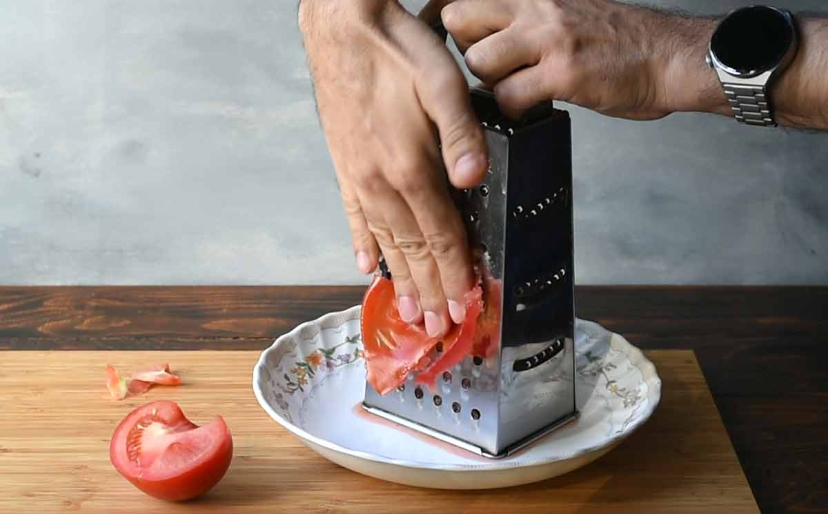 A hand grating a tomato on a box grater.