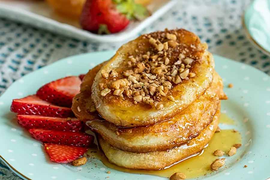 A stack of tiganites on a plate with sliced strawberries, honey and nuts.