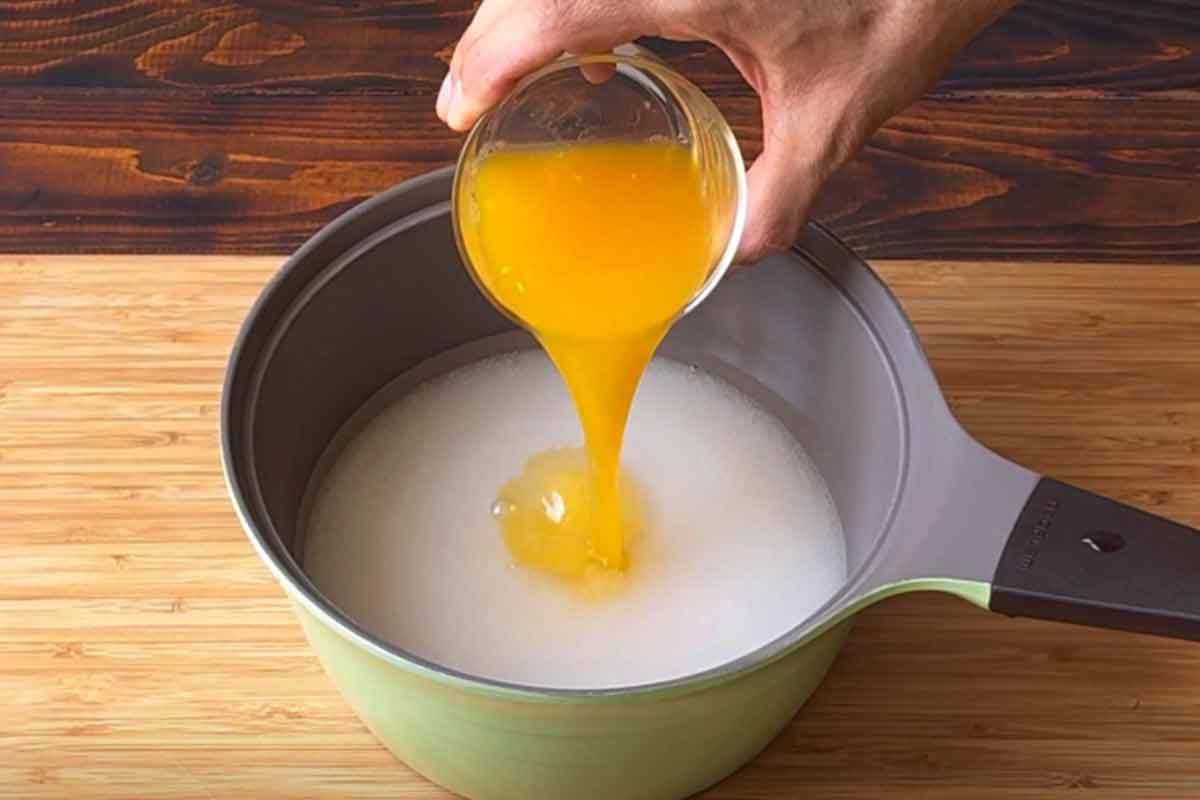 A hand adding orange juice to a pot with water and sugar.