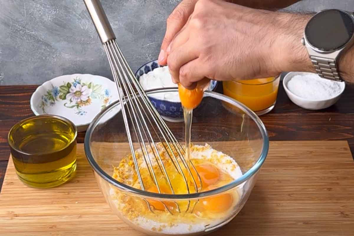Two hands breaking an egg over the bowl with the sugar mixture.