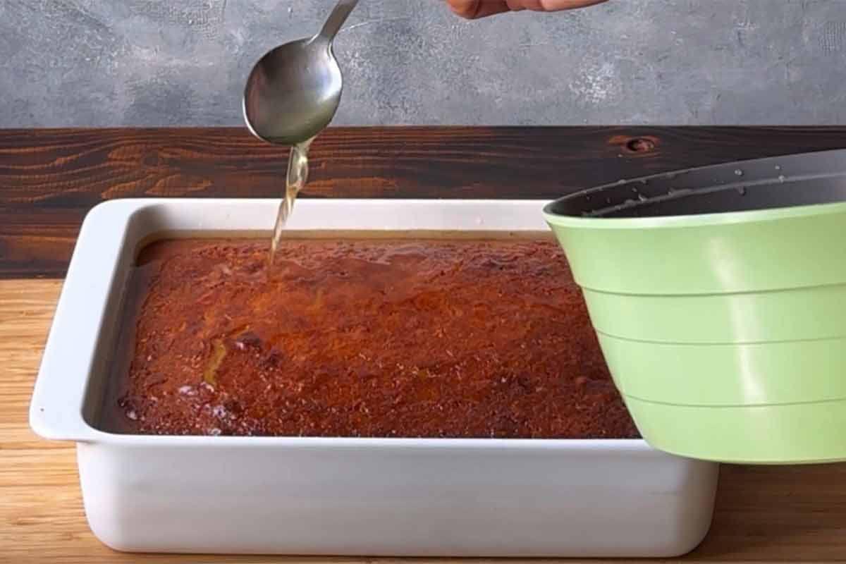 Spooning the cooled syrup over the hot cake.