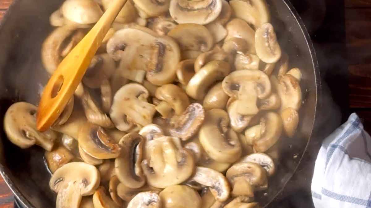 A hand stirs chopped mushrooms in a skillet.
