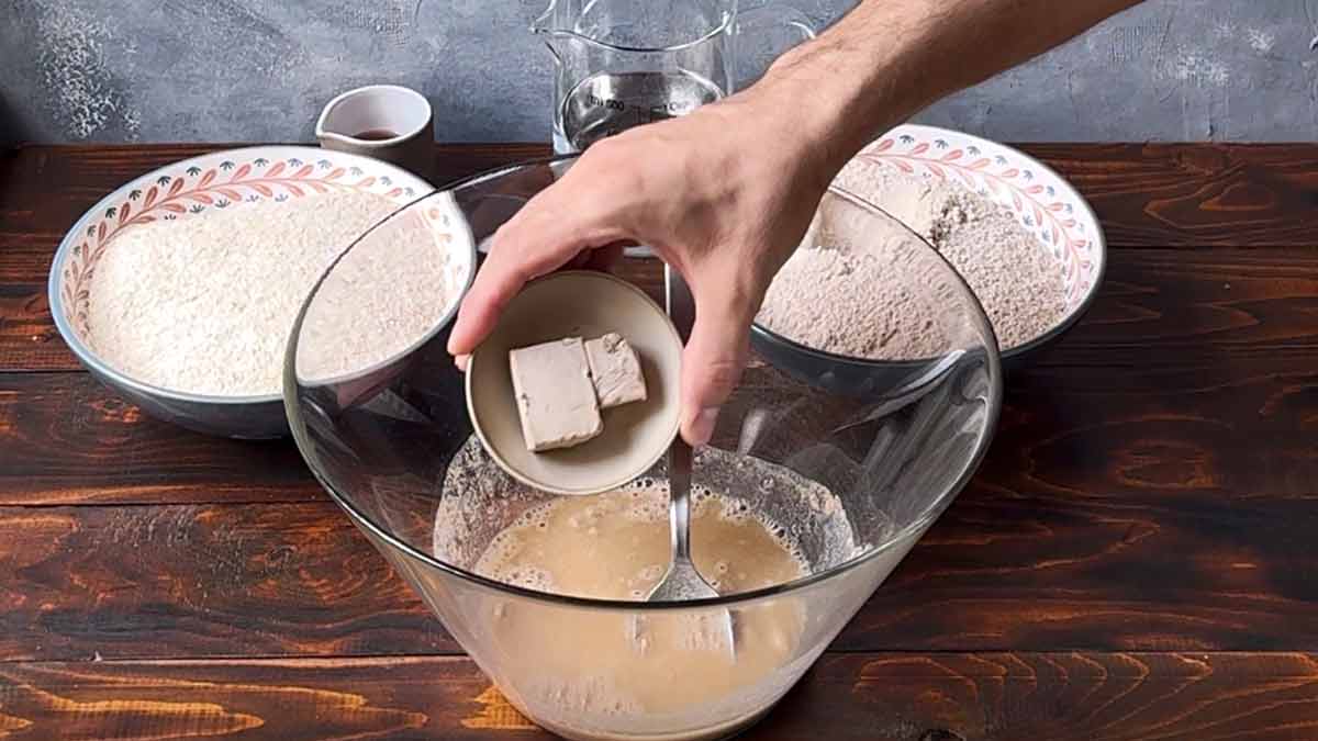 A hand dissolving fresh yeast in water.