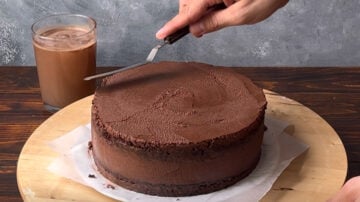 A hand smoothing the chocolate frosting with an offset spatula.